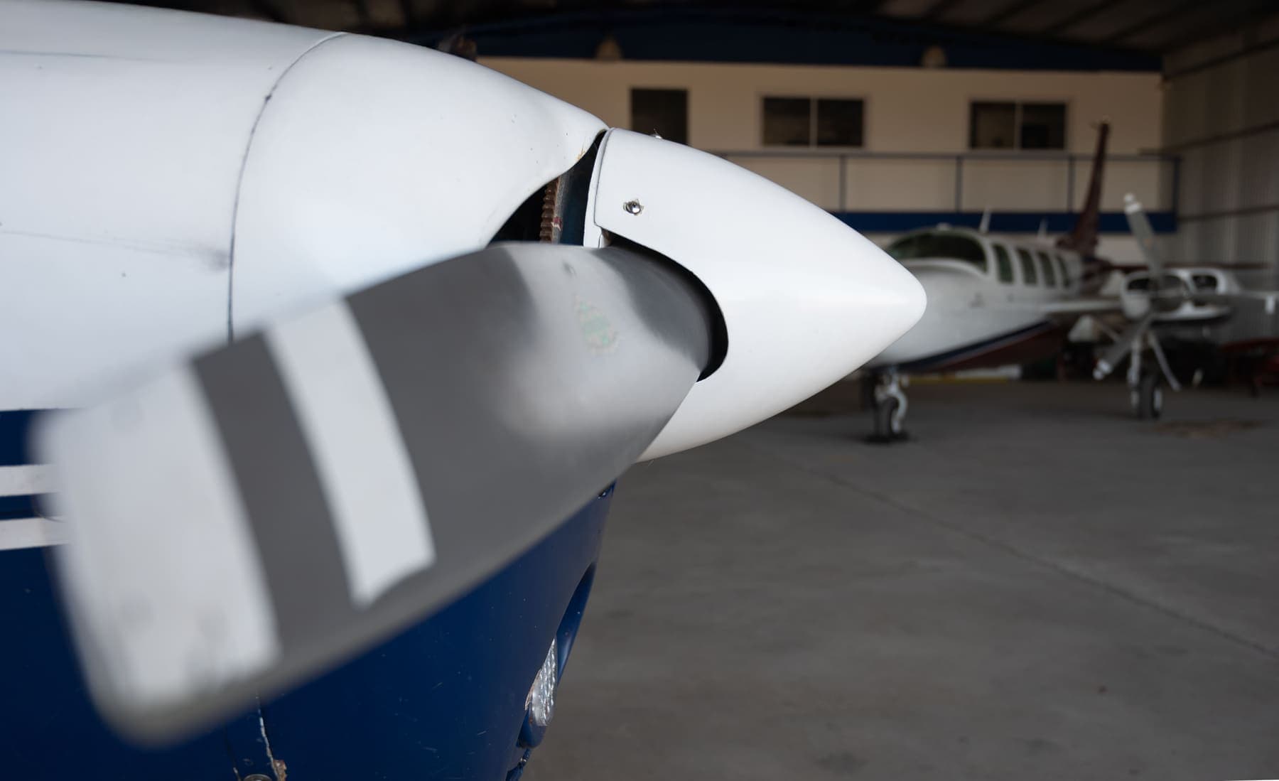 Close view of a piston twin's propeller blade and spinner in the hangar, another twin waiting behind