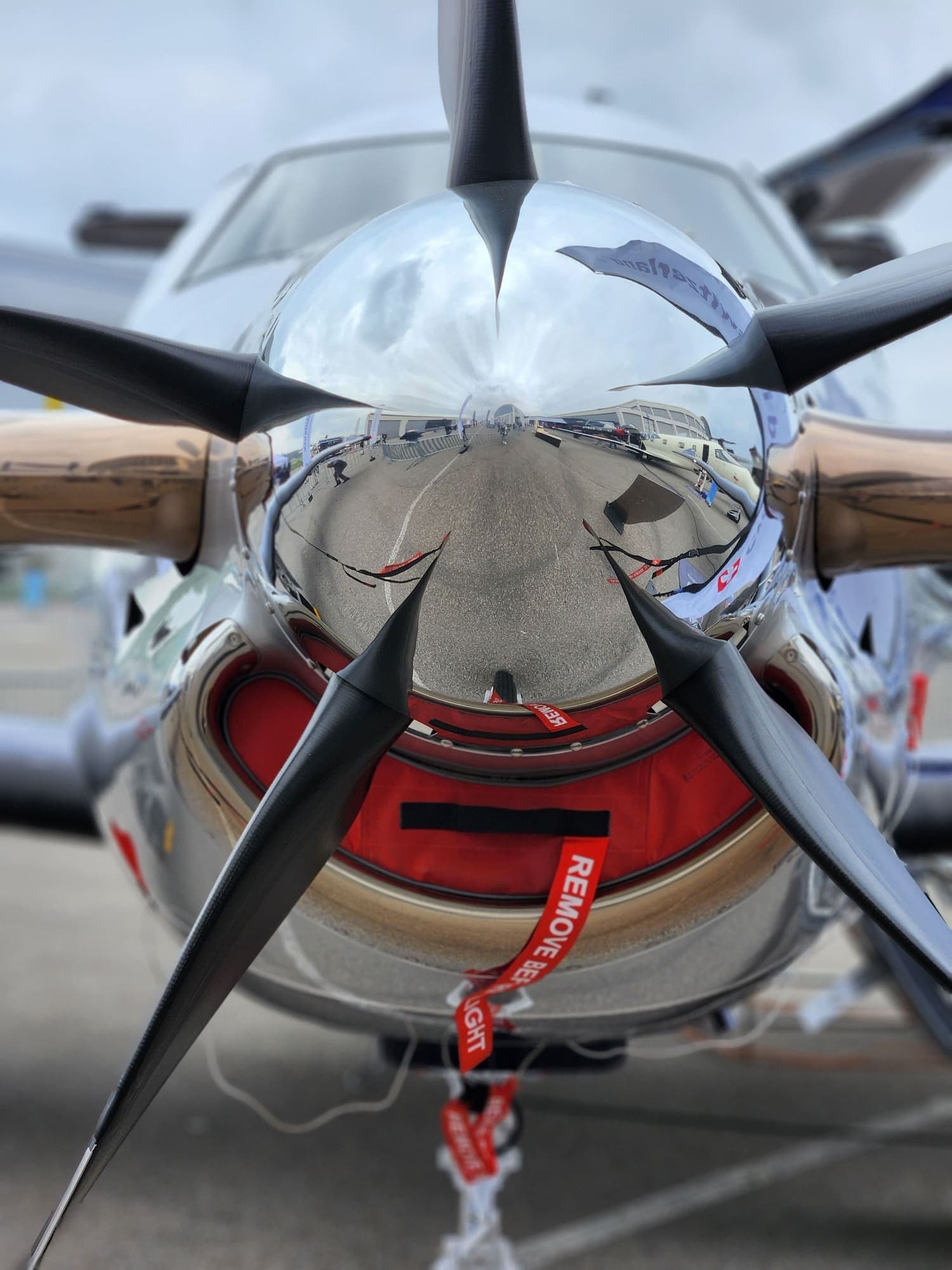 A turboprop propeller spinner polished to a full mirror finish, reflecting the whole apron around it