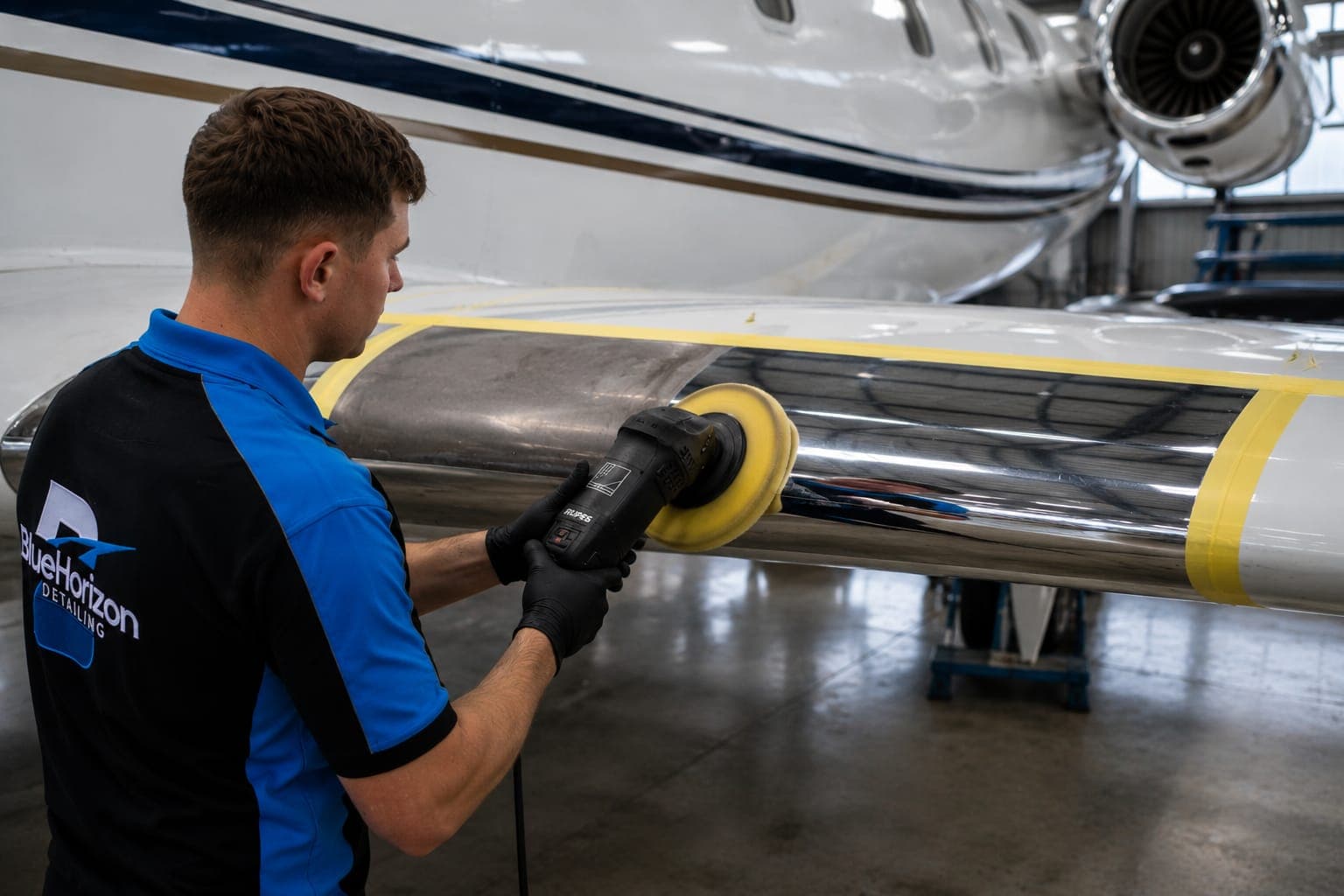 A Blue Horizon technician machine-polishing a masked leading edge, half restored to mirror brightwork